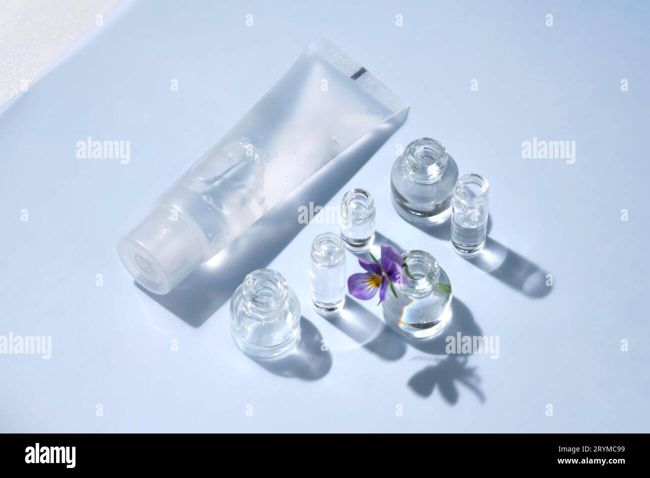 Transparente Flasche kosmetisches Gel auf blauem Hintergrund mit kleinen Flaschen Wasser. Stockfoto