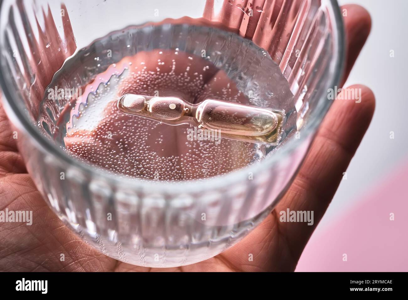 Ampulle in einem Becher mit Wasser auf rosa Hintergrund. Das Symbol der Luftbefeuchtung. Stockfoto