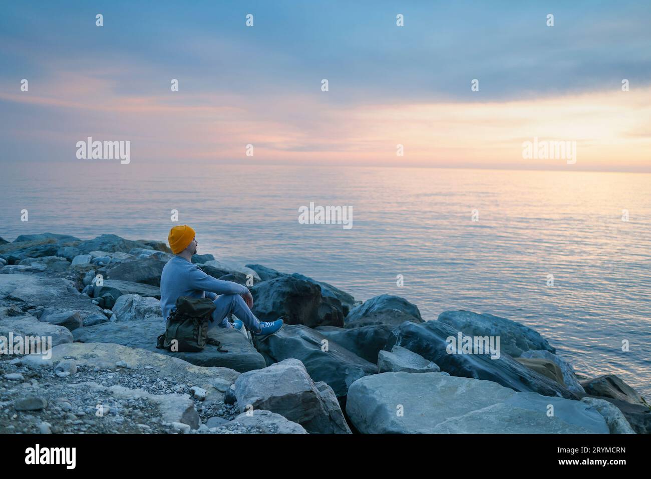 Ein Aukasier mit blauem Pullover und Hut hält seinen Rucksack und schaut auf das ruhige Meer. Stockfoto