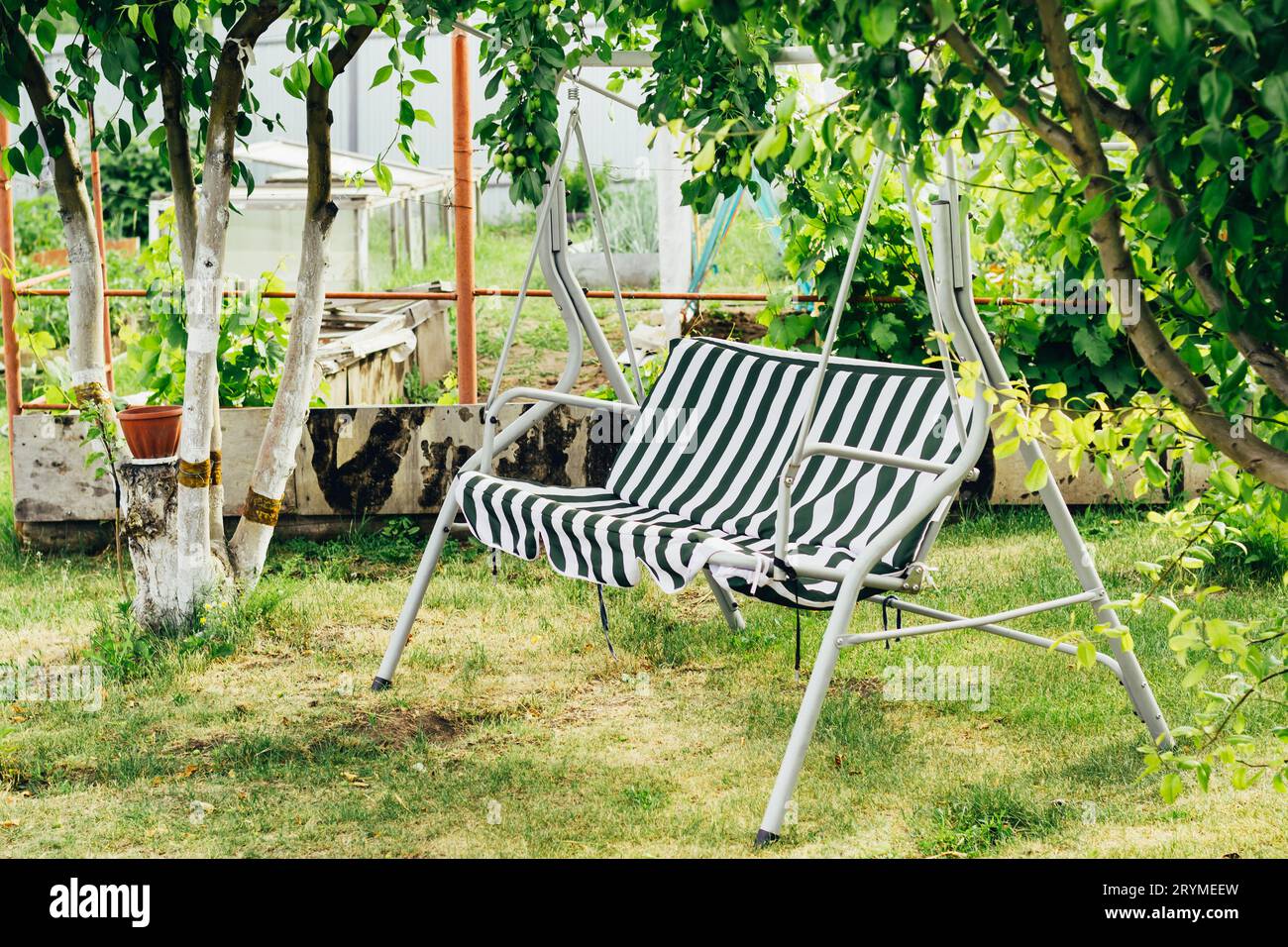 Schwingen Sie zwischen Bäumen im Garten. Cottagecore und Staycation zu Hause. Sommergarten mit Platz für Erholung und Entspannung Stockfoto