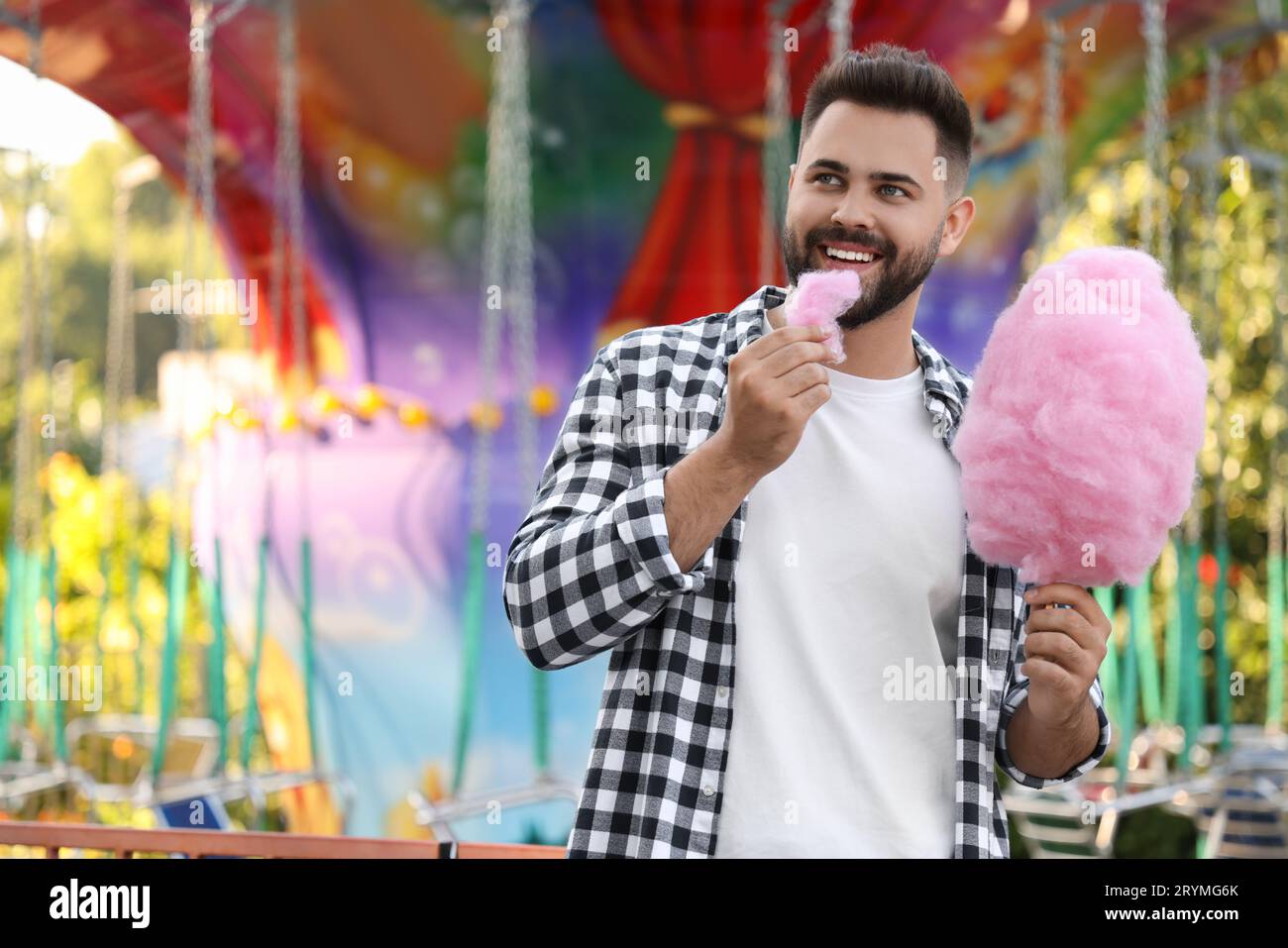 Glücklicher junger Mann, der auf der Messe Zuckerwatte isst, Platz für Text Stockfoto
