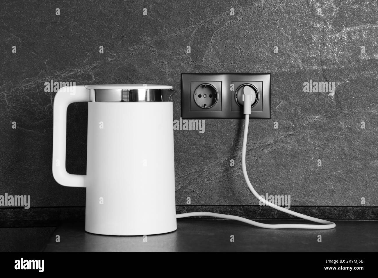 Elektrischer Wasserkocher, der an eine Steckdose an einer dunkelgrauen Wand im Innenbereich angeschlossen ist Stockfoto