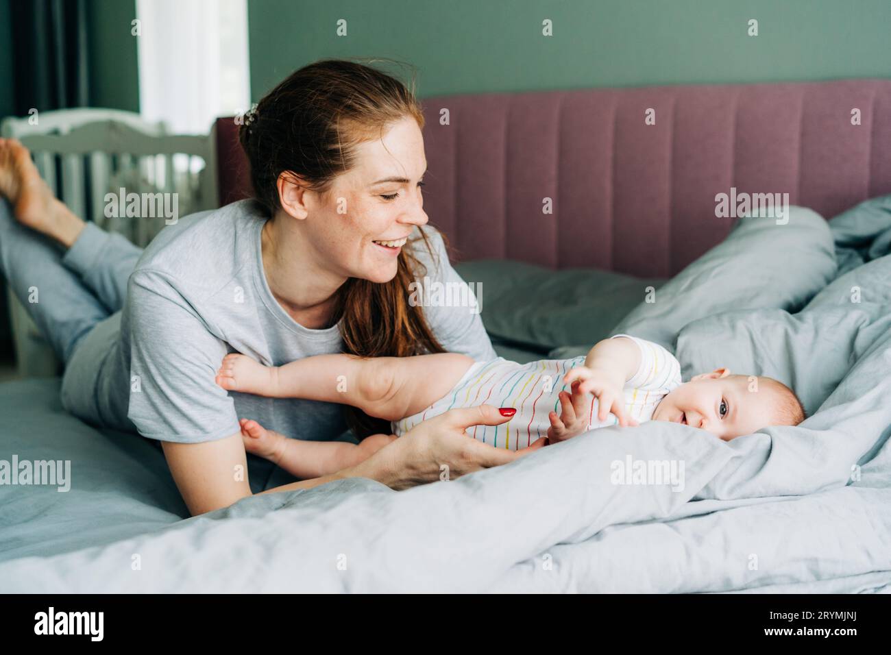 Junge Mutter hat Spaß beim Spielen mit dem Baby im Bett. Eine fürsorgliche Mutter erziehen eine neugeborene Tochter. Stockfoto