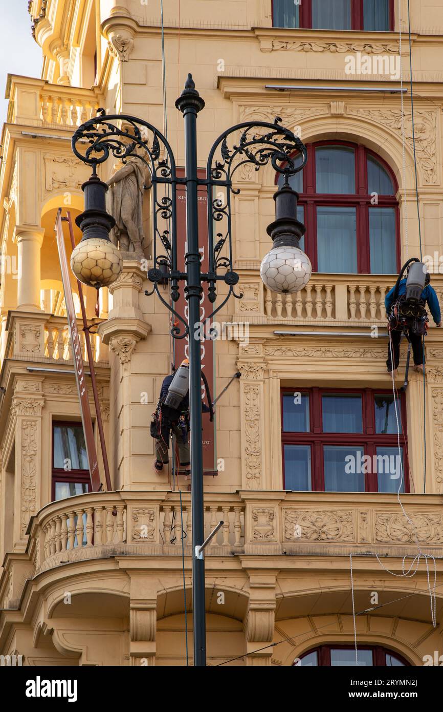 Prag, CZ - 28. oktober 2021:zwei Arbeiter mit Staubsaugern, die hoch oben auf der Rupe hängen und Staub an der Fassade eines Hotels in Prag reinigen. Sauber Stockfoto