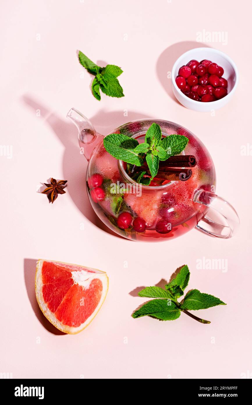Immunitätssteigerungsgetränk. Minztee mit Preiselbeeren, Grapefruit und Gewürzen in Glas-Teekanne auf rosa Tisch, trendige Schatten Stockfoto