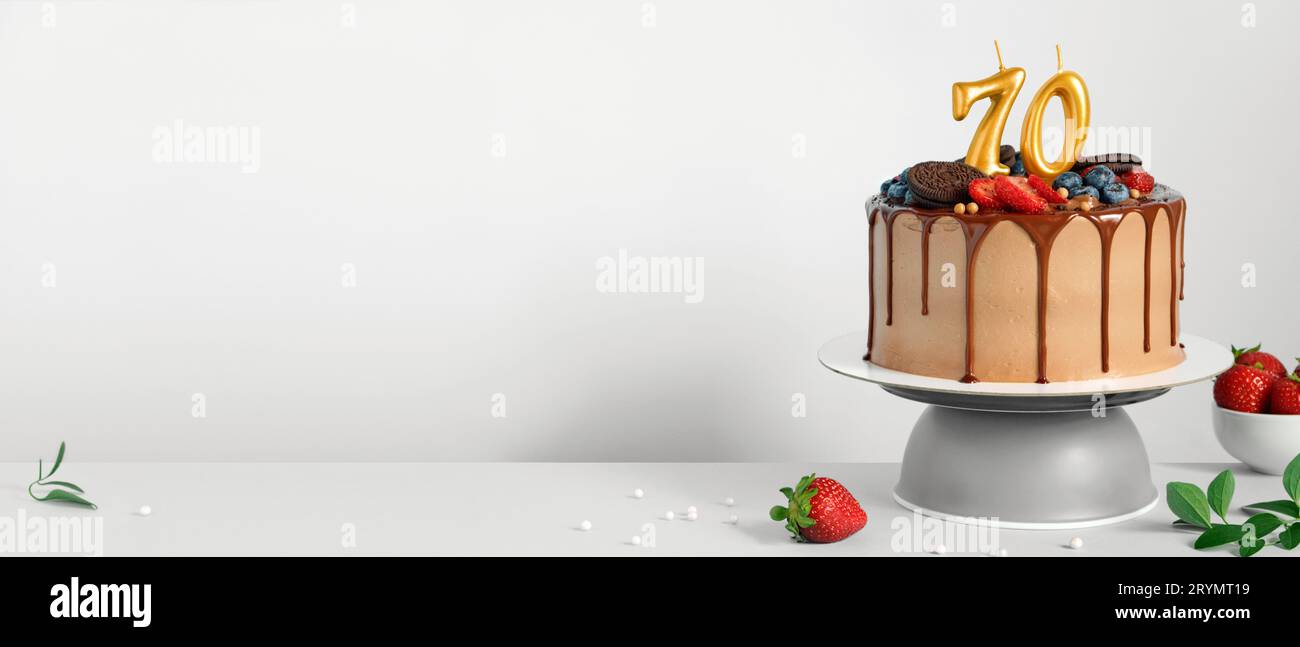 Banner mit Schokolade Geburtstagskuchen mit Beeren, Keksen und Zahl siebzig goldene Kerzen auf weißem Hintergrund, Kopierraum Stockfoto