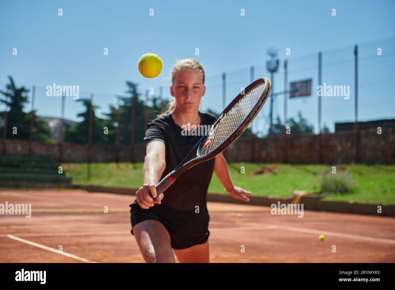 Ein junges Mädchen, das professionelle Tennisfähigkeiten in einem Wettkampf an einem sonnigen Tag zeigt, umgeben von der modernen Ästhetik von A Stockfoto