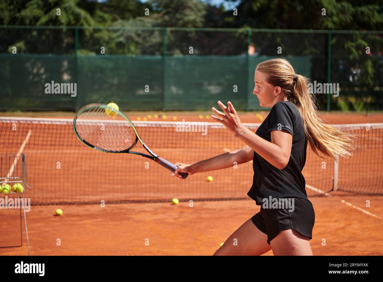 Ein junges Mädchen, das professionelle Tennisfähigkeiten in einem Wettkampf an einem sonnigen Tag zeigt, umgeben von der modernen Ästhetik von A Stockfoto