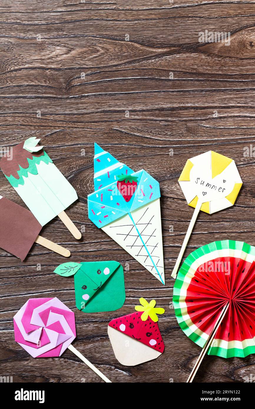 Lustiger Spielzeuglutscher, Wassermelone, Eis und Lesezeichen Erdbeere und Apfel. Sommerspielzeug aus Papier, Holzstäbchen auf einem Holztisch. Stockfoto