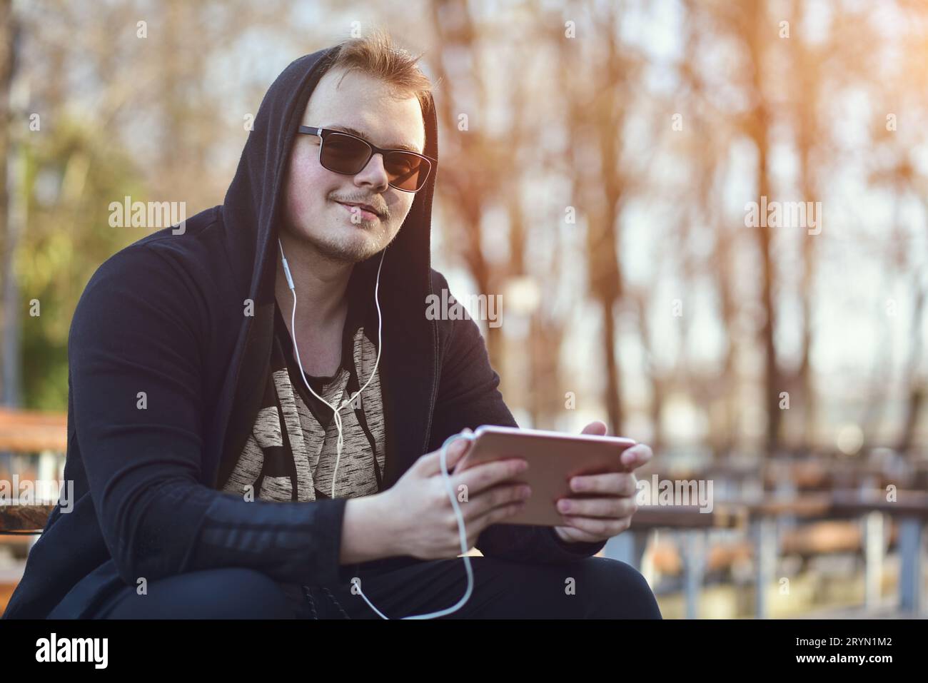 Ein Mann mit einem Tablet-Computer sitzt in einem Freiluftpark. Stockfoto