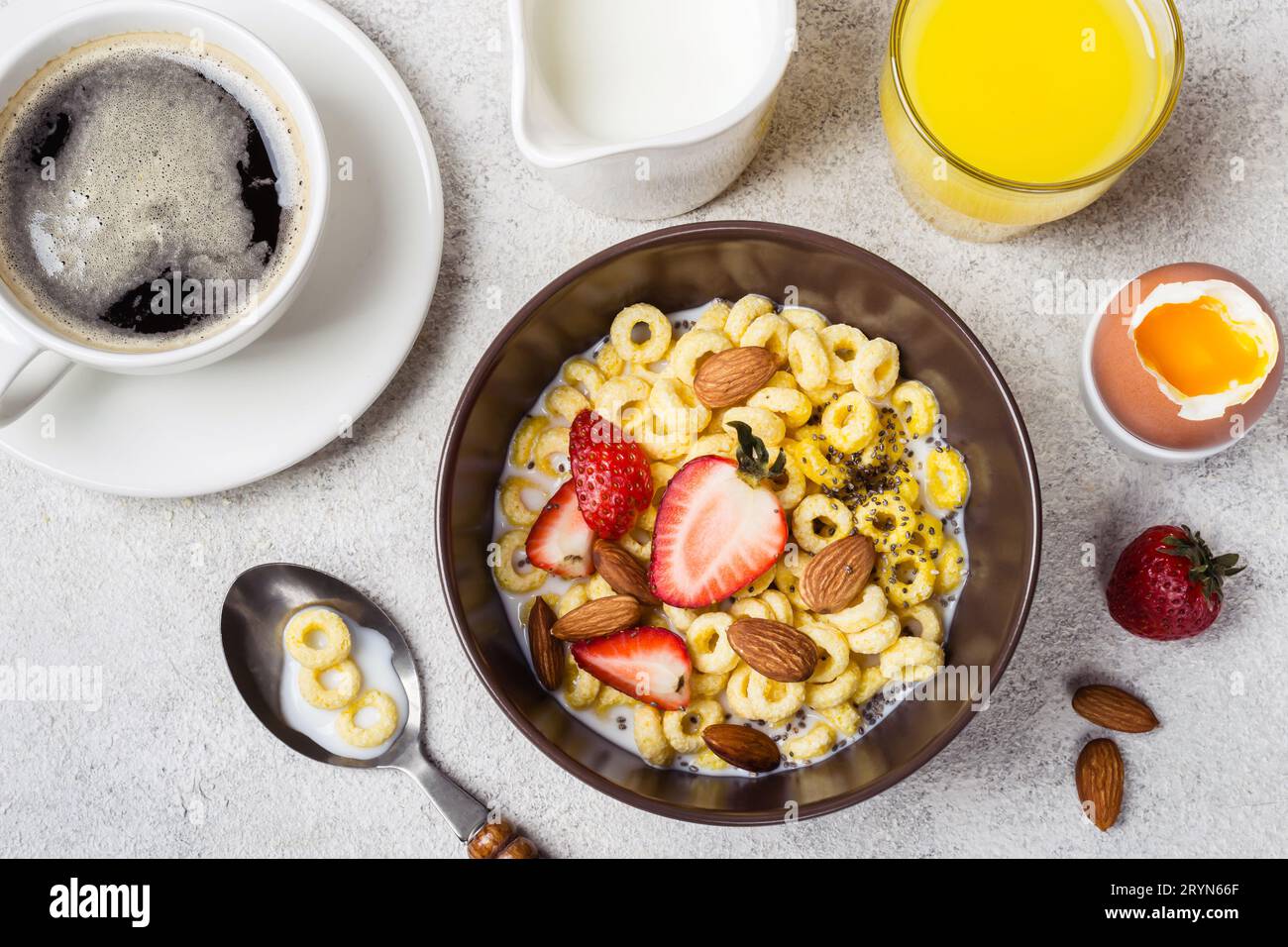 Schüssel mit Müsliringen, Cheerios, Erdbeeren und Milch. Frischer Kaffee, Orangensaft und Ei. Ausgewogenes Frühstückskonzept Stockfoto