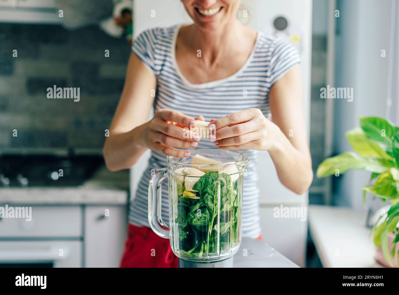 Eine junge Frau gibt die Zutaten für einen Smoothie in eine Mixschüssel. Gesunde Ernährung Konzept. Stockfoto