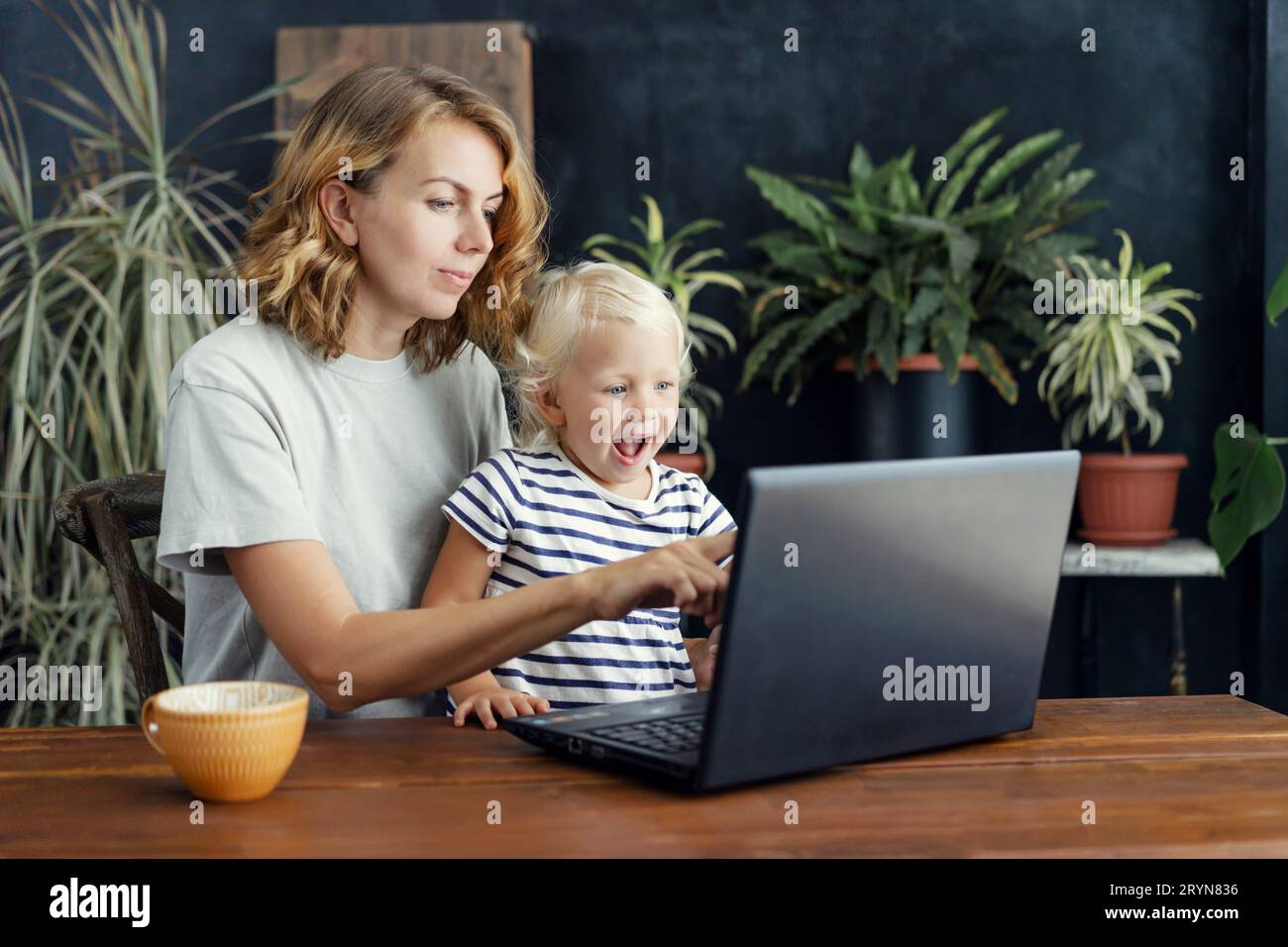 Kleine komisch überraschte Tochter und Mutter schauen sich einen Laptop an. Kindliche Unschuld und offene Gefühle. Lifestyle Familienportr Stockfoto