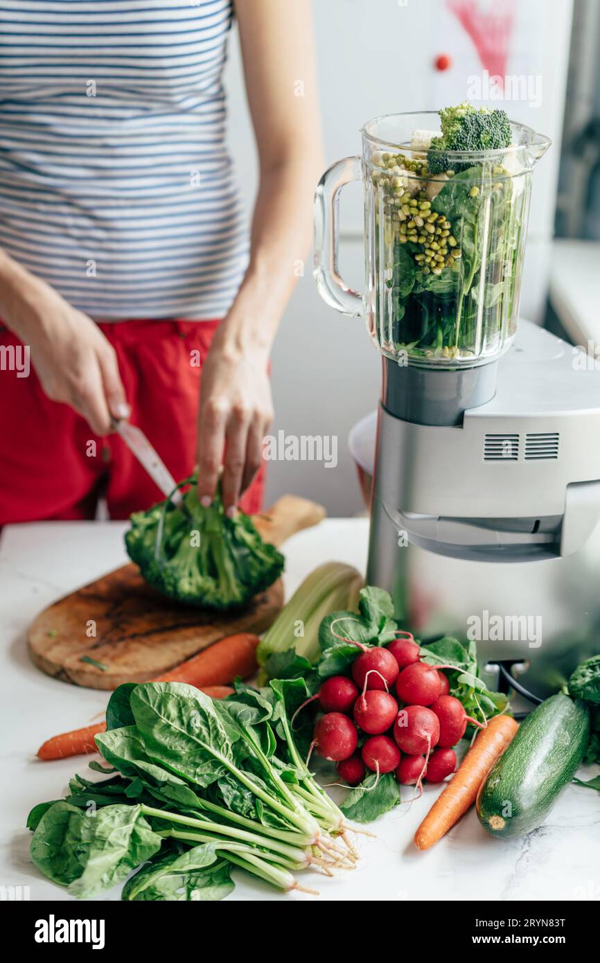 Vertikales Bild. Frau schneidet Zutaten für einen gesunden Snack. Salat und Smoothie kochen. Stockfoto