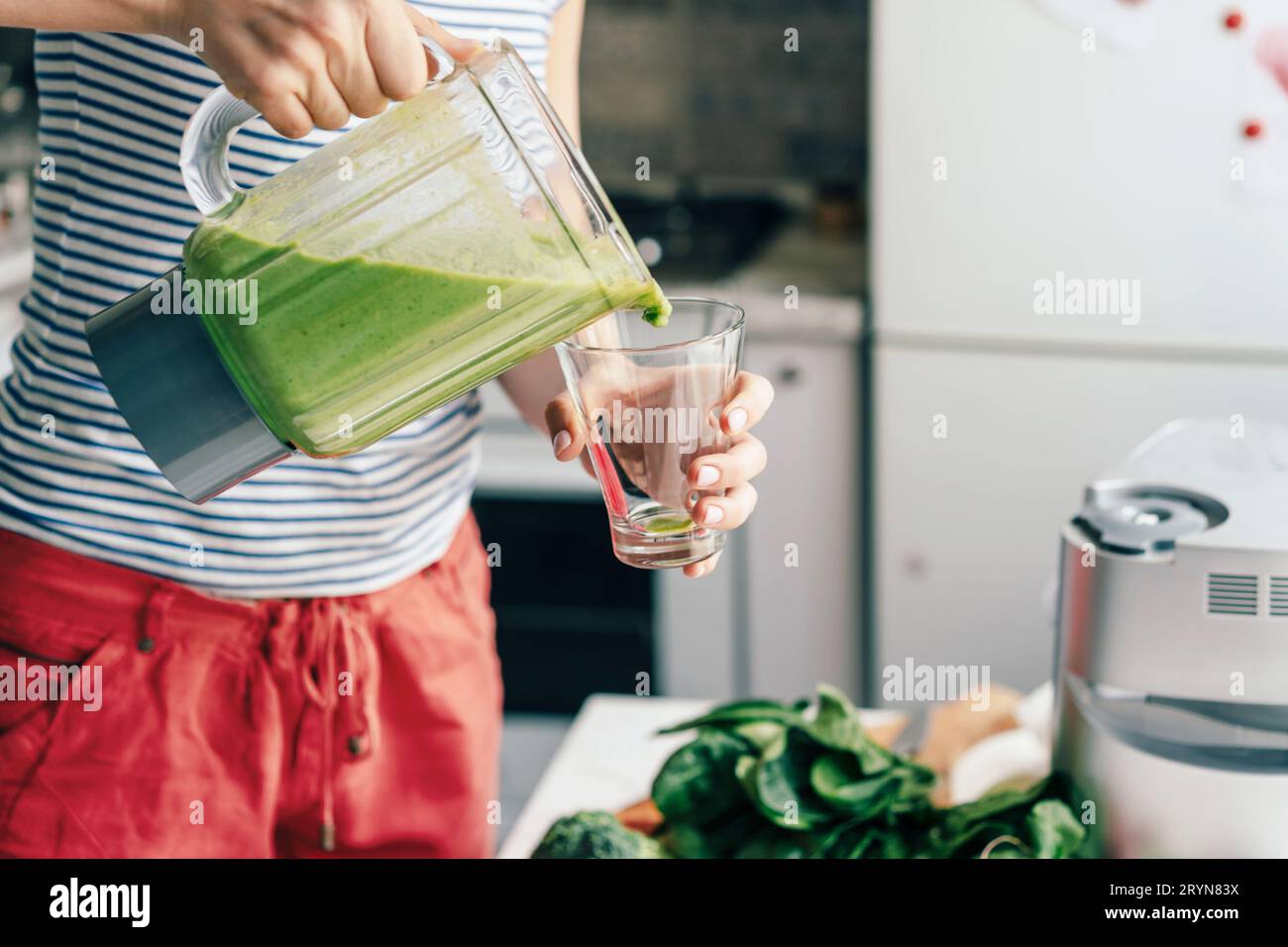 Eine Frau gießt einen Smoothie aus einem Vitamincocktail in ein Glas. Gesundheitskoch zu Hause. Lifestyle Stockfoto