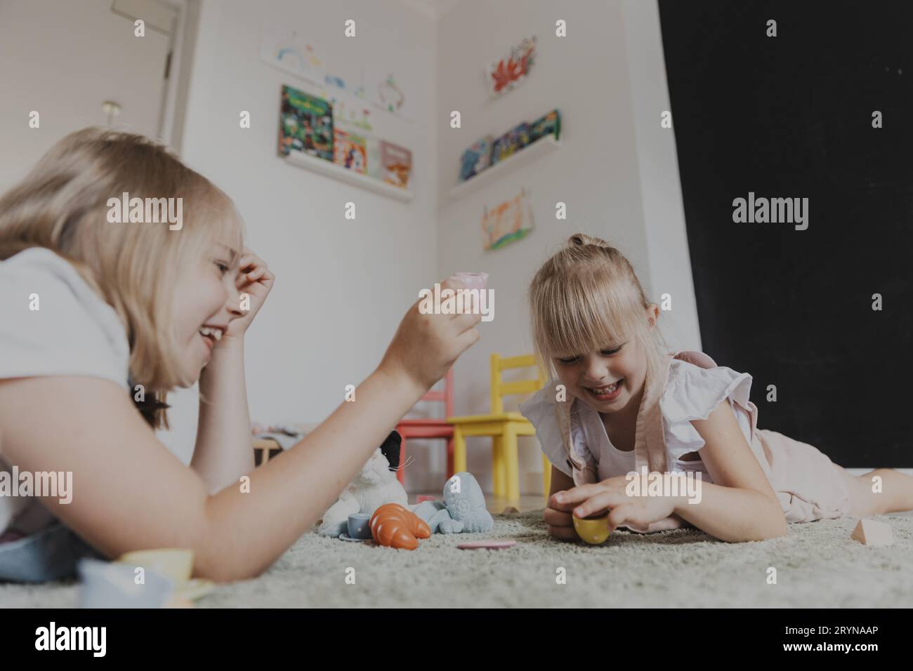 Nahaufnahme von weiblichen Kindern, die mit farbenfrohem Spielzeug in der Küche spielen, Teeset spielen. Kinder sitzen auf Teppich im Schlafzimmer oder Kindergarten, Kinderzimmer. Bildungswesen Stockfoto