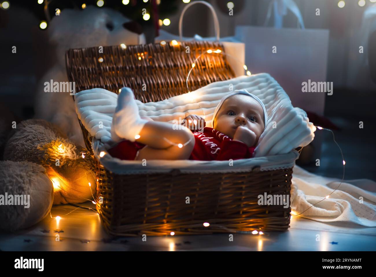 Kleine Rutschbaby mit weihnachtskleidung in Korb weihnachtsdekoration und Blitzlicht um sie herum. Stockfoto