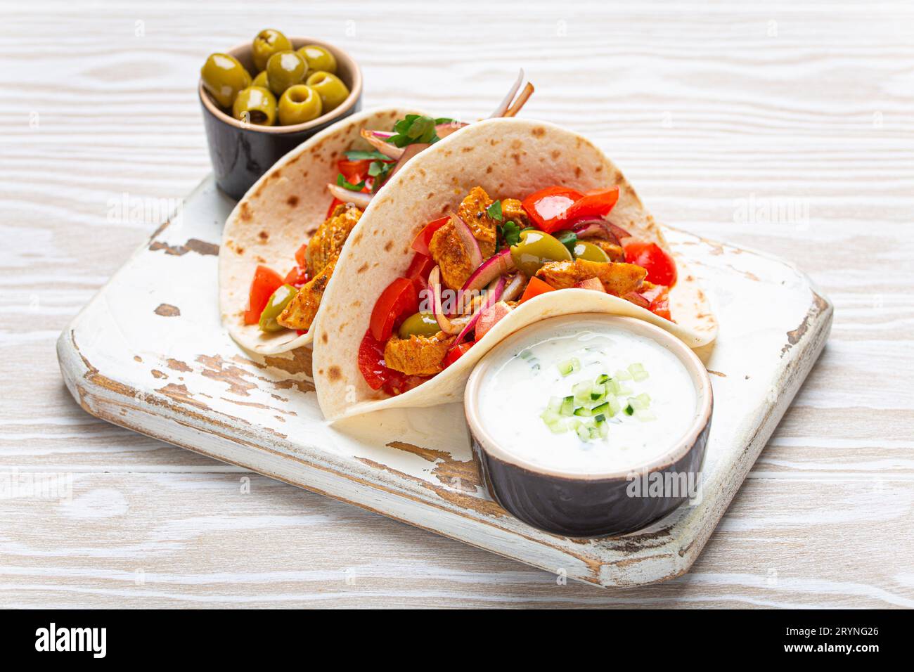 Traditionelles griechisches Gericht Gyros: Pita Brotwickel mit Gemüse, Fleisch, Kräutern, Oliven auf rustikalem Holzschneidebrett mit Tzatziki Stockfoto
