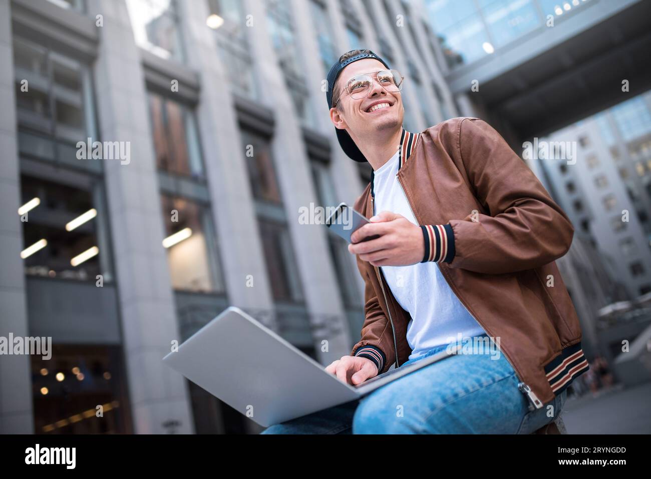 Clevere Einstellung. Ein gutaussehender Mann, der einen Laptop benutzt und auf der Straße sitzt, während er im Internet surft, hat eine Webkonferenz. Stockfoto