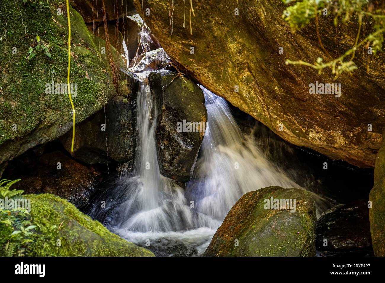Nahaufnahme eines malerischen kleinen Wasserfalls, der durch große moosbedeckte Felsen in einen tropischen Pool taucht Stockfoto