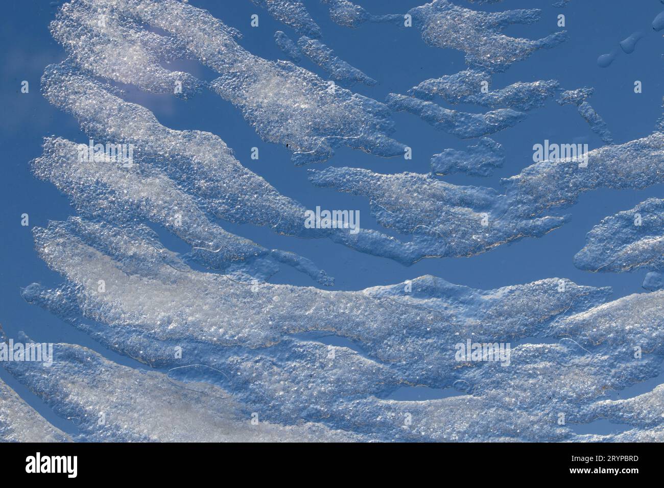 Schmelzender Schnee und Eis bilden wolkenartige Muster auf einem Dachfenster unter einem blauen Winterhimmel Stockfoto