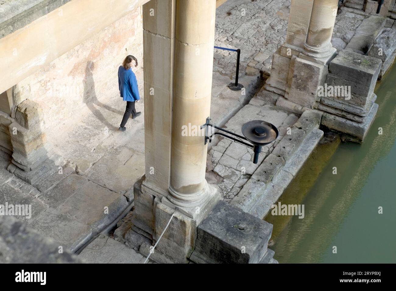 Ein Mitarbeiter von Roman Bath wirft einen Schatten auf eine Wand, während sie an einer Säule des Great Bath im Roman Bath's, Bath, Somerset, Großbritannien vorbeigeht Stockfoto