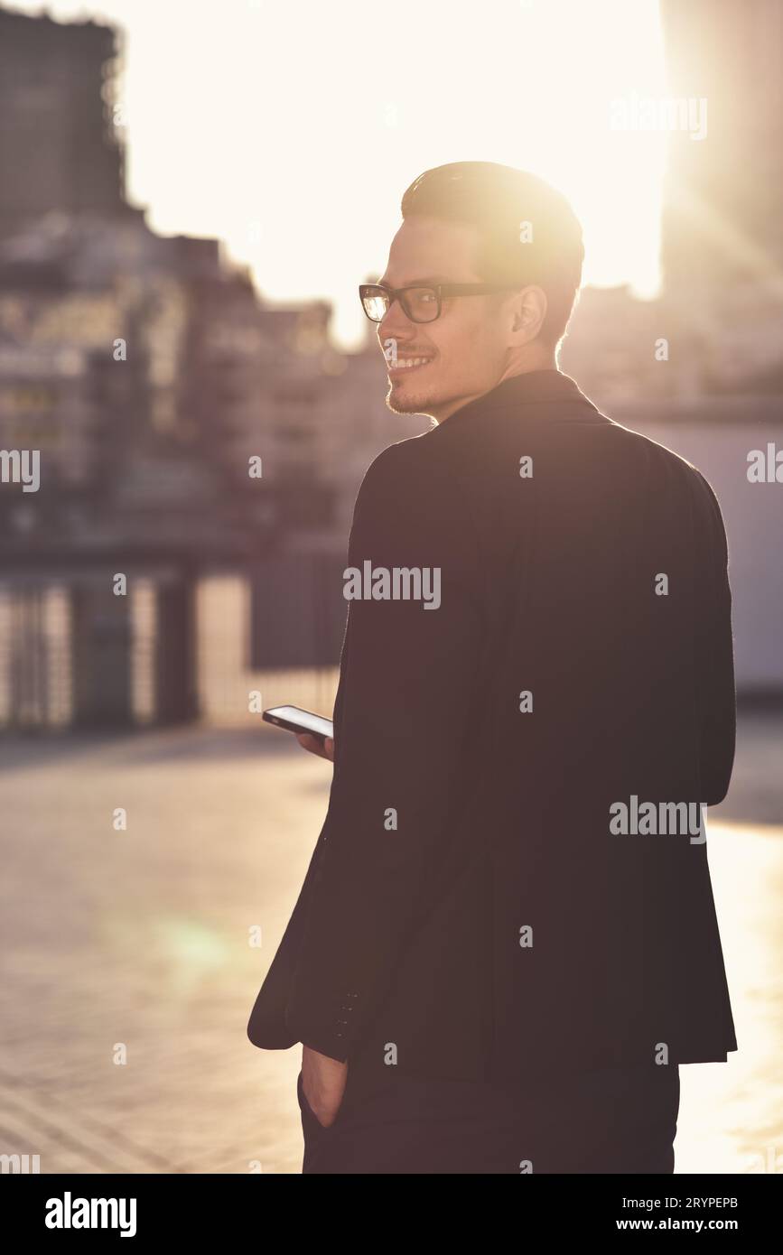 Erfolgreicher Geschäftsmann in Brille steht mit Telefon in einer modernen Stadt. Stockfoto