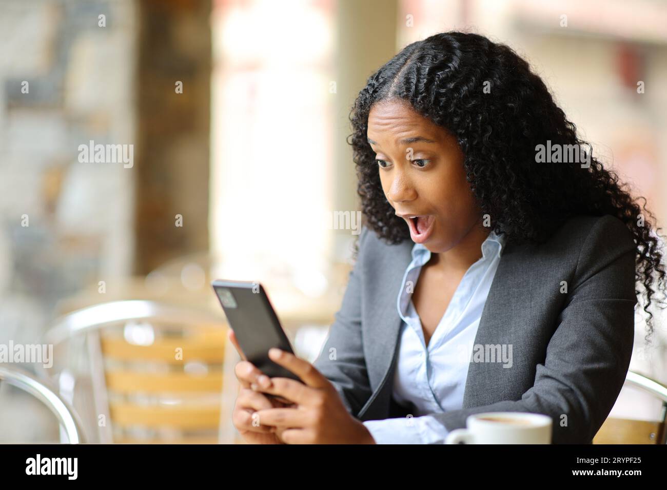 Verblüffter schwarzer Manager, der das Smartphone auf einer Bar-Terrasse überprüft Stockfoto