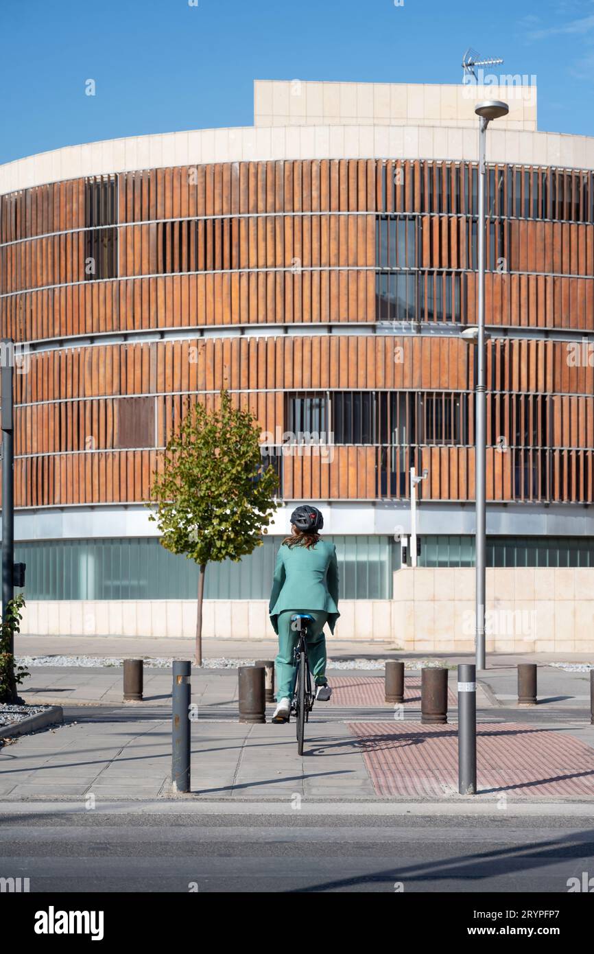 Stilvolle Geschäftsfrau im grünen Anzug, schwarzer Helm, der auf dem Fahrrad auf der Straße fährt Stockfoto