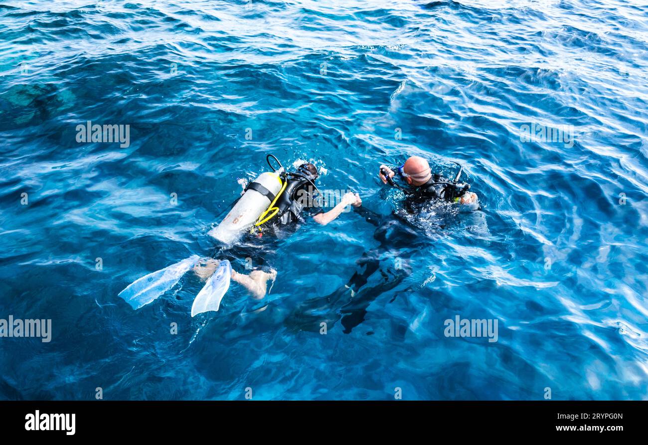 Tauchlehrer hält die Hand eines Schülers in blauem Wasser Stockfoto