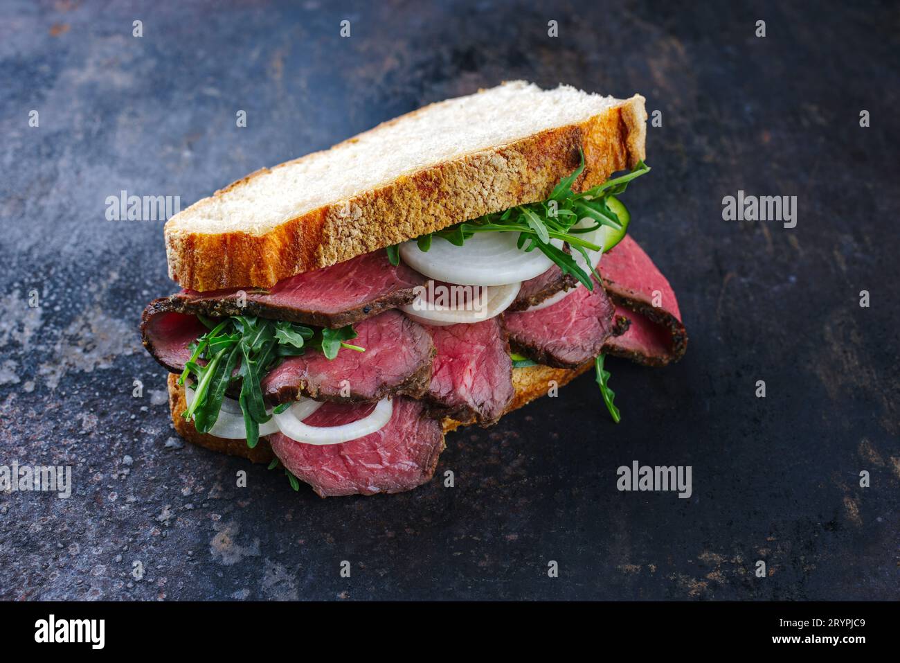 Traditionelles Roastbeef-Sandwich mit Raketensalat und Zwiebelringen, serviert mit italienischem Ciabatta-Brot als Nahaufnahme auf einem alten Ru Stockfoto