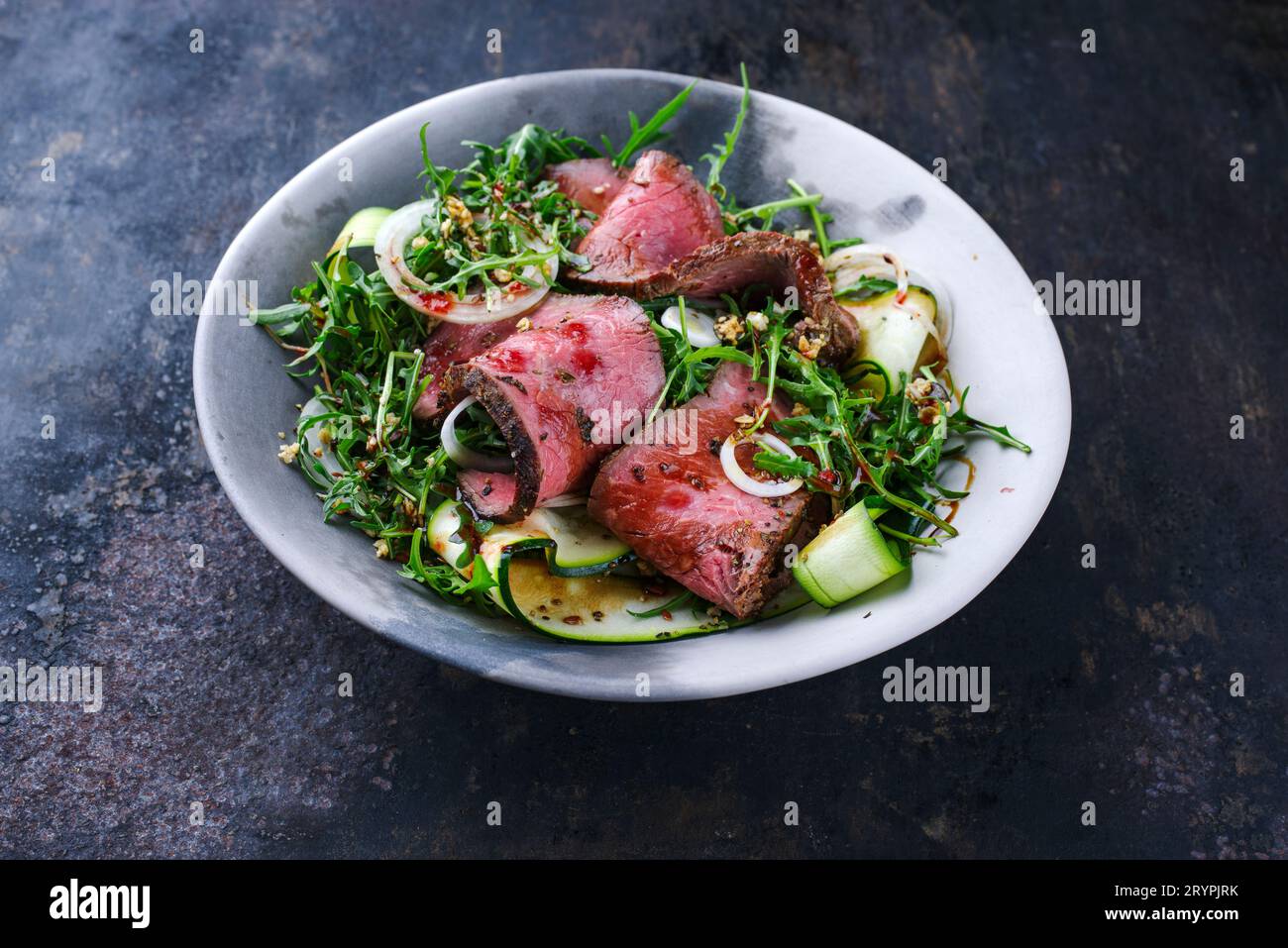 Traditioneller Commonwealth-Sonntagsbraten als in Scheiben geschnittene Wurst Roastbeef mit Zucchini und Zwiebelringen in Raketensalat serviert Stockfoto