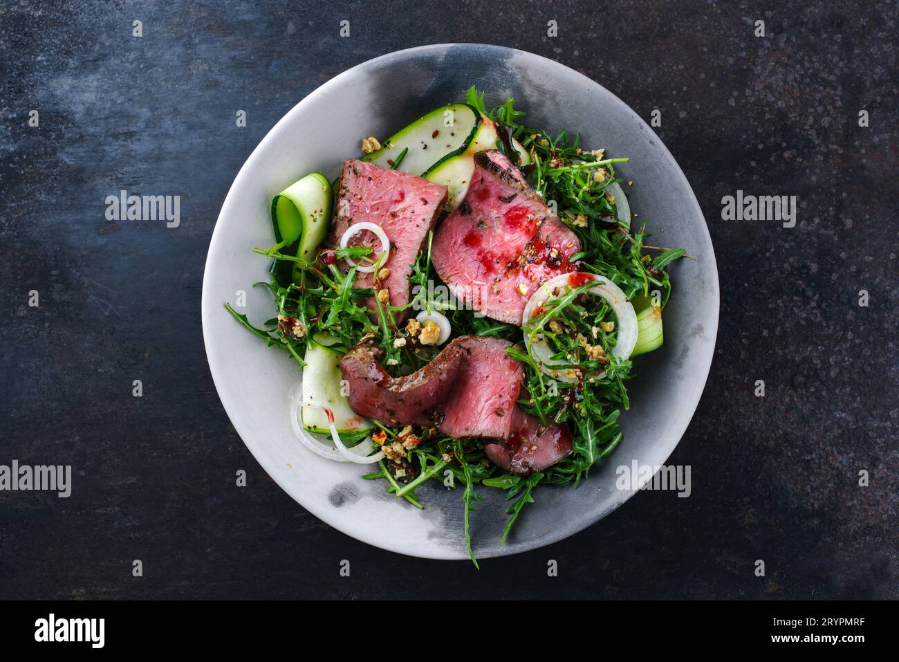 Traditioneller Commonwealth-Sonntagsbraten als in Scheiben geschnittene Wurst Roastbeef mit Zucchini und Zwiebelringen in Raketensalat serviert Stockfoto