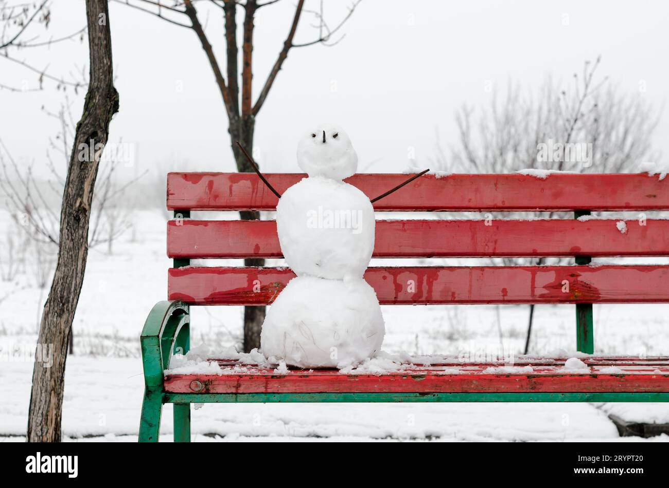 Gruseliger Schneemann auf einer roten Bank in einem verschneiten einsamen Park Stockfoto