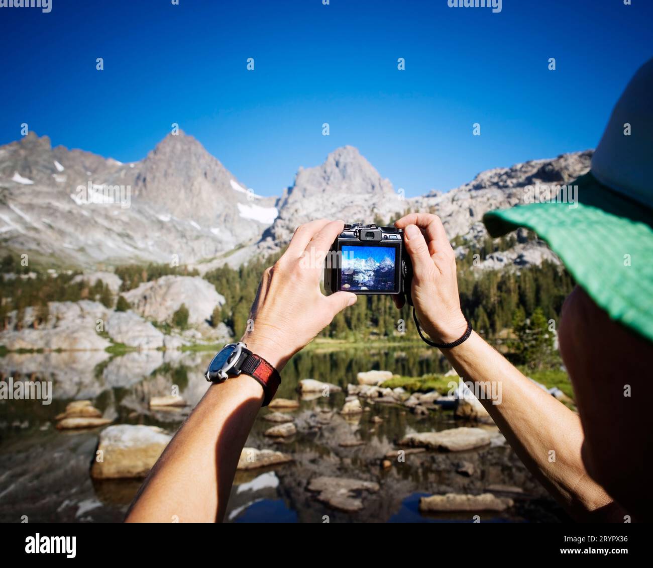 Blick über die Schulter einer Backpackerin, die ein digitales Foto von einem Bergbach und einer Wiese macht. Stockfoto