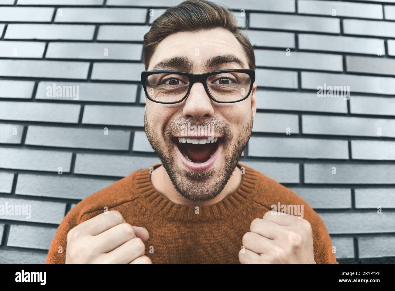 Nahaufnahme überrascht Mann in Brillen Blick auf Kamera und offenen Mund auf Backstein Hintergrund. Stockfoto