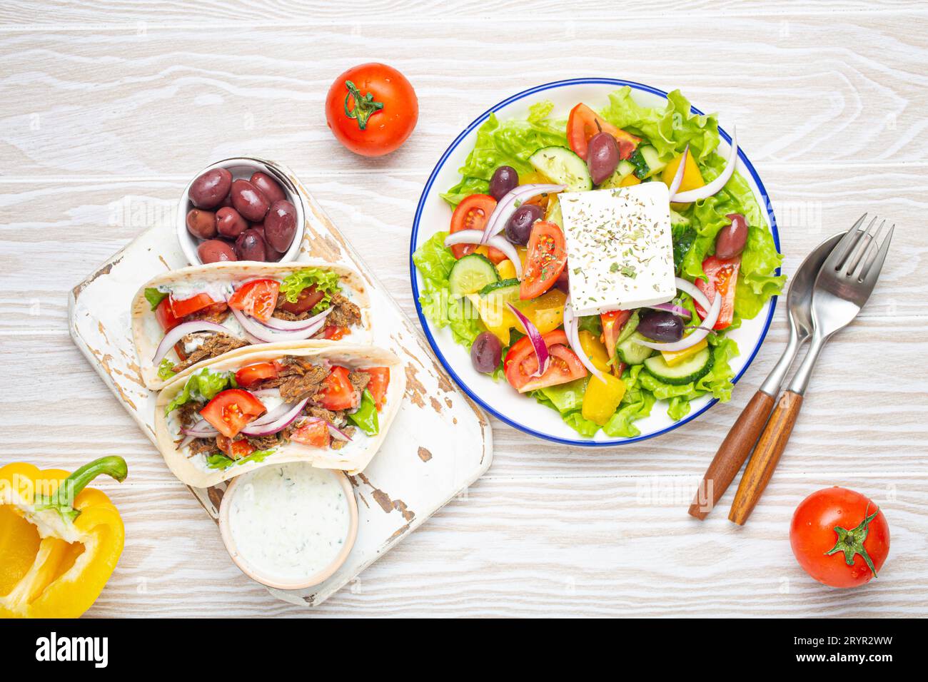 Traditionelles griechisches Essen: Griechischer Salat, Gyros mit Fleisch und Gemüse, Tzatziki-Sauce, Oliven auf weißem rustikalem Holztisch Stockfoto