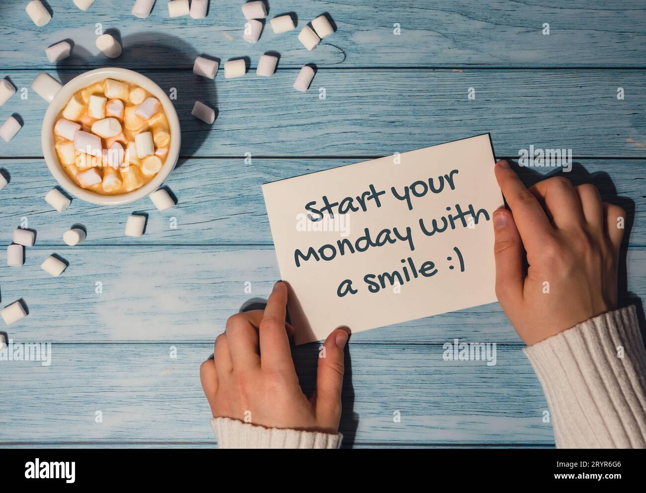 BEGINNEN SIE IHREN MONTAG MIT Einem LÄCHELN Konzepttext weibliche Hände halten Karte mit weißer Tasse Kaffee und Marshmallows auf hölzernem Backgr Stockfoto