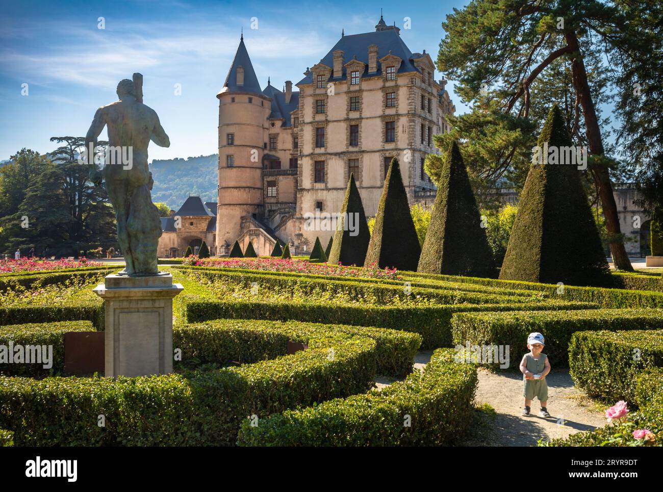Ein kleiner Junge steht neben einer großen Statue in den formellen Gärten des Schlosses, in dem sich das Museum der Französischen Revolution in Vizille befindet. Stockfoto