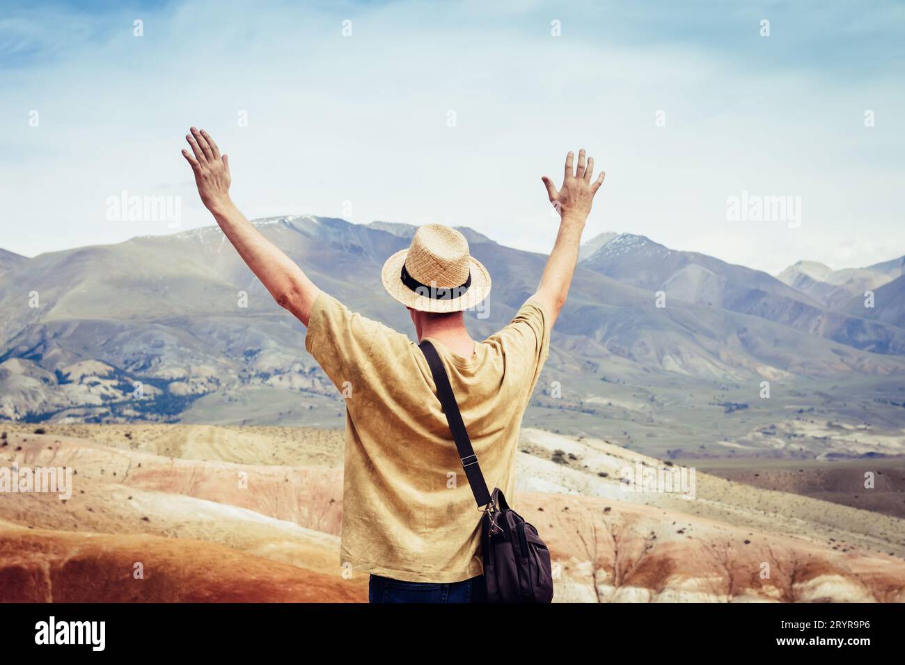 Männlicher Tourist mit offenen Händen steht auf einem Berg und blickt auf eine Bergkette Stockfoto