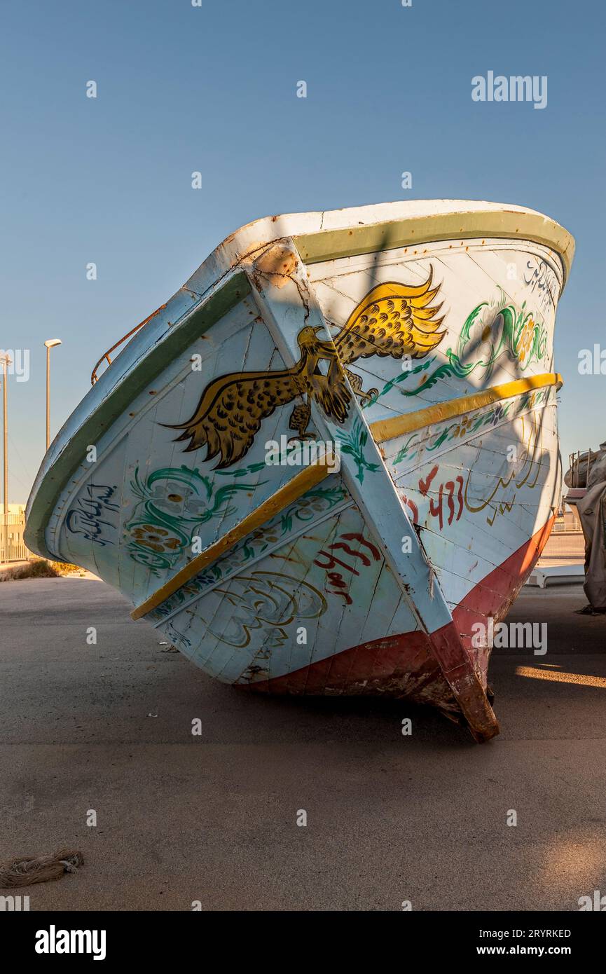 Alte Fischerboote, die von Flüchtlingen und Migranten genutzt wurden, um das Mittelmeer von Nordafrika nach Europa zu überqueren, von italienischen Grenzbeamten beschlagnahmt und im Hafen von Pozzallo, Sizilien, Italien, gelagert. Die gemalten Symbole (insbesondere das Horusauge) sollen Glück bringen und das Böse abwehren. Stockfoto