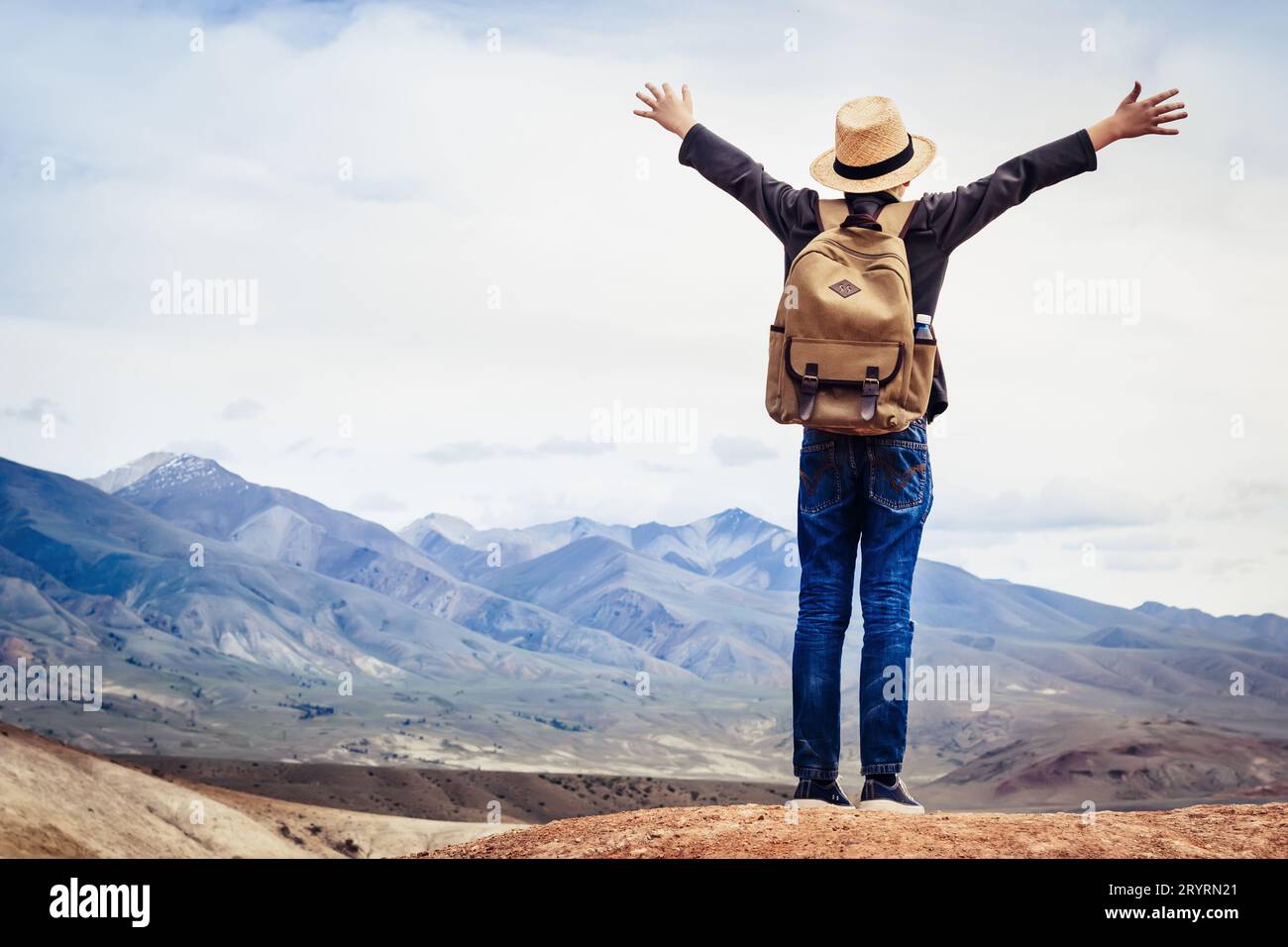 Reisender Junge mit Rucksack und Strohhut blickt auf die Berge Stockfoto