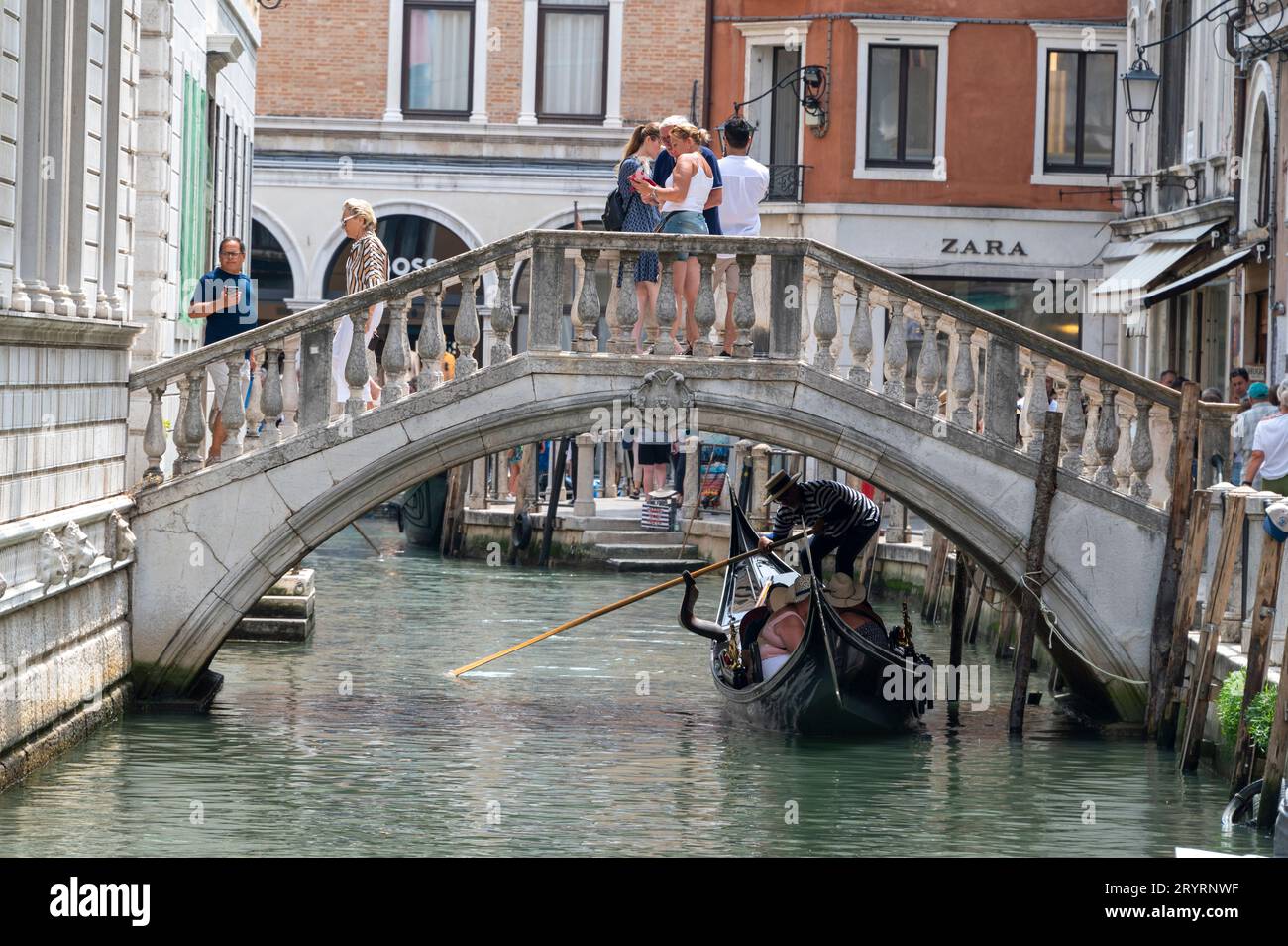 Ein Gondolier lenkt seine Gondel unter einer der vielen niedrigen Fußgängerbrücken in den Canale Grande in der Nähe der Rialto-Brücke in Venedig in der Region Veneto Stockfoto