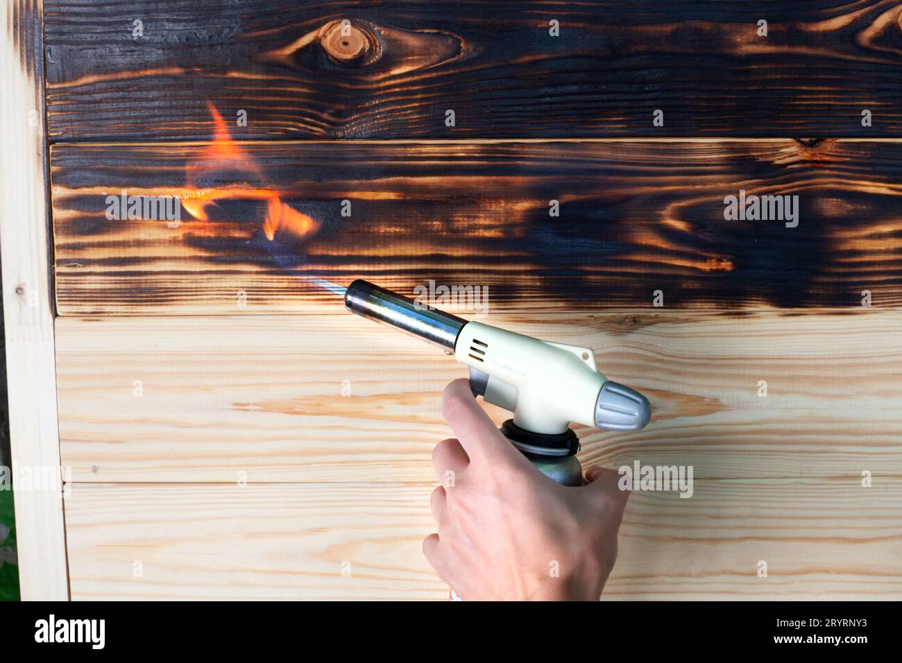 Holzbrettverbrennung mit Gasbrenner. Bürsten mit einem Gasbrenner zu Hause. Behandeln des weichen Holzes mit Feuer. Dekoration von Holzprodukten. Stockfoto