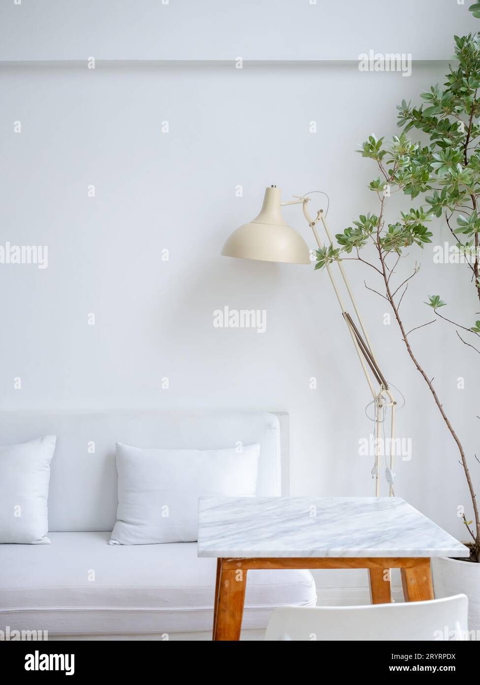 Moderne, entspannende und saubere Wohnzimmerecke mit weißer Couch oder Sofasessel mit Kissen, beige Tischlampe neben leerem Marmortisch Stockfoto