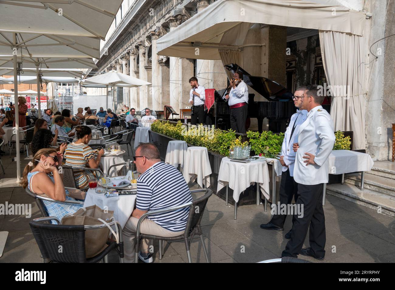Zwei weiße Garderobe-Kellner in der Nähe einer Live-Band treten bei sitzenden Gästen im Caf Florian auf dem Markusplatz in Venedig auf Stockfoto