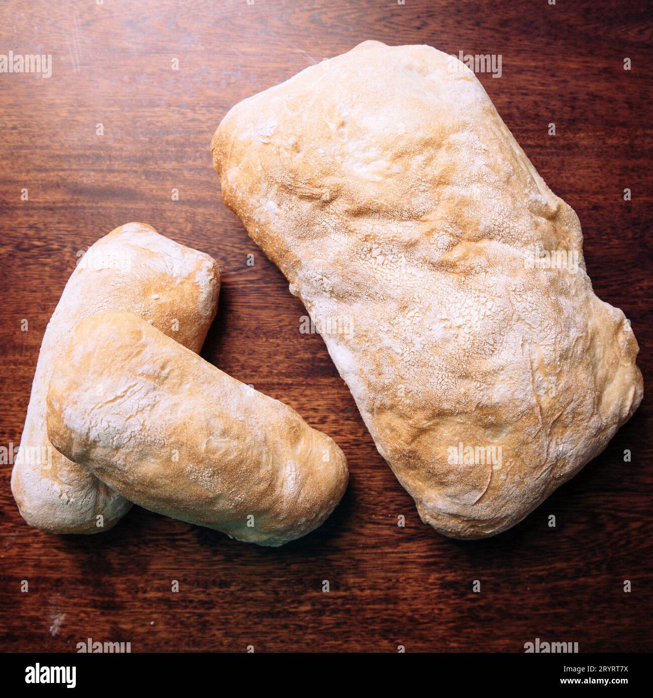 Ein frisch geschnittenes Brot, das neben zwei kleineren Brötchen auf einem Holztisch steht Stockfoto