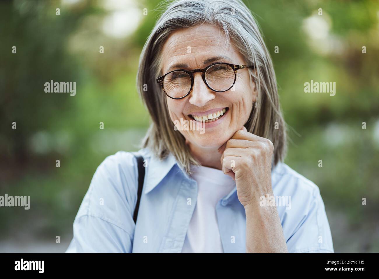 Ältere Frau mit grauen Haaren lächelt im Park. Ein echter Moment des Glücks und der Freude, während die Frau eine ruhige Umgebung im Park genießt. Sie Stockfoto