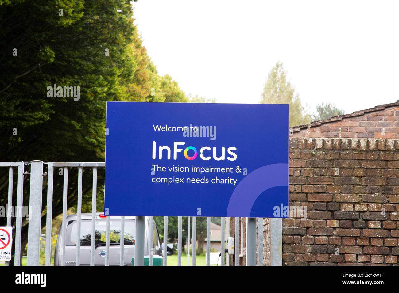 InFocus Sehbehinderung und Komplex benötigt blaue Beschilderung für wohltätige Zwecke mit Bäumen im Hintergrund Stockfoto