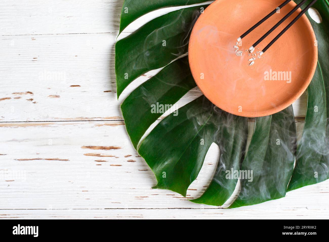 Brennende aromatische Räucherstäbchen. Keramikschale und Monsterblatt Stockfoto